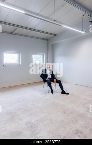 Homme d'affaires assis sur une chaise dans une salle éclairée Banque D'Images
