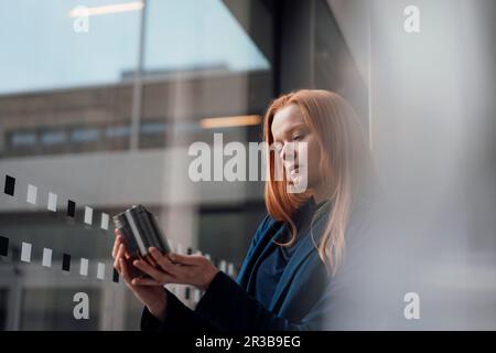 REDHEAD femme d'affaires analysant une pièce de machine à la fenêtre Banque D'Images