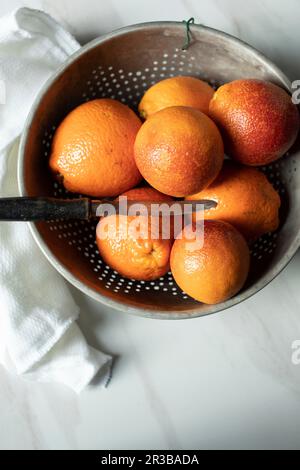 Des oranges de sang dans une passoire avec un couteau Banque D'Images