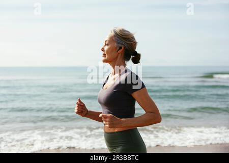 Femme d'âge mûr avec écouteurs intra-auriculaires sans fil à la plage Banque D'Images