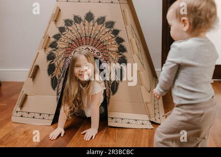 Frères et sœurs jouant avec une tente en carton à la maison Banque D'Images