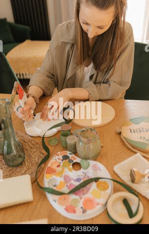 Jeune femme versant de la peinture dans la palette à la maison Banque D'Images