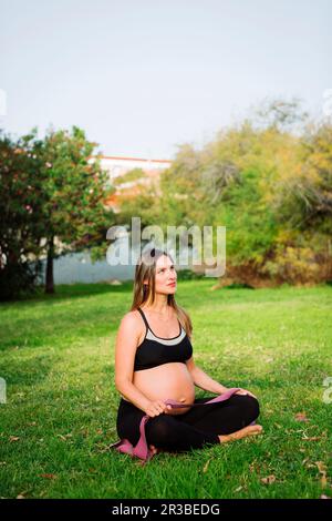 Femme enceinte réfléchie assise sur une pelouse Banque D'Images