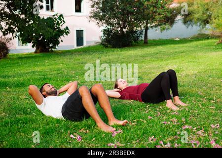 Femme enceinte s'exerçant avec un homme allongé sur l'herbe Banque D'Images