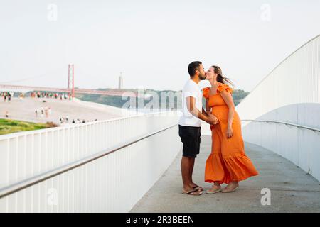 Femme enceinte embrassant homme debout près de la main courante sur le sentier Banque D'Images