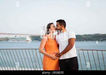 Femme enceinte embrassant l'homme devant la main courante Banque D'Images