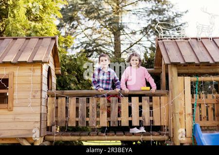 Frères et sœurs se tenant sur une passerelle en bois près d'une maison de jeu dans la cour arrière Banque D'Images