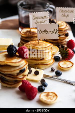 Des piles de mini-crêpes avec des pancakes, avec des fruits et des chips de chocolat, du sirop et du beurre, sur un plateau en marbre Banque D'Images