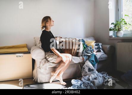 Femme attentionnés assise sur un canapé avec linge encombré à la maison Banque D'Images