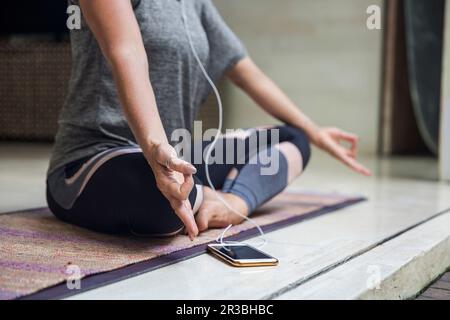 Femme pratiquant Lotus position assise croisée par smartphone à la maison Banque D'Images