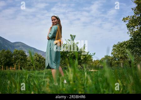 Femme avec des oranges dans un sac en maille debout dans un verger Banque D'Images