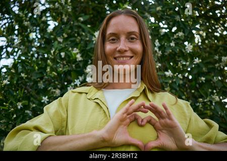 Femme souriante faisant un geste de coeur dans le jardin Banque D'Images