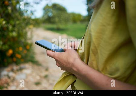 Messagerie texte de femme via smartphone dans le jardin Banque D'Images