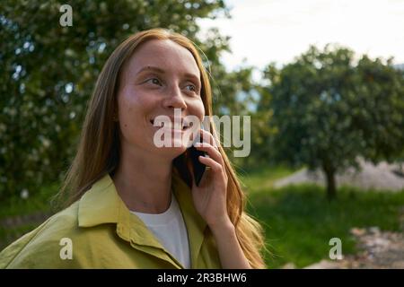Femme contemplative parlant sur un smartphone dans le jardin Banque D'Images