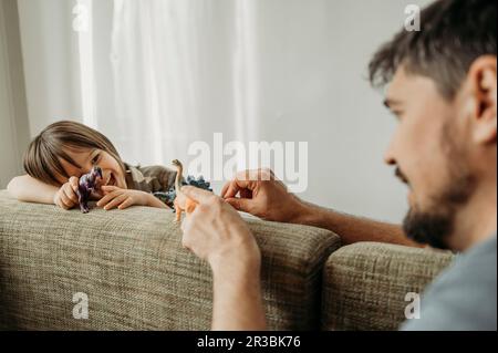Père et fils jouant avec des dinosaures sur le canapé à la maison Banque D'Images