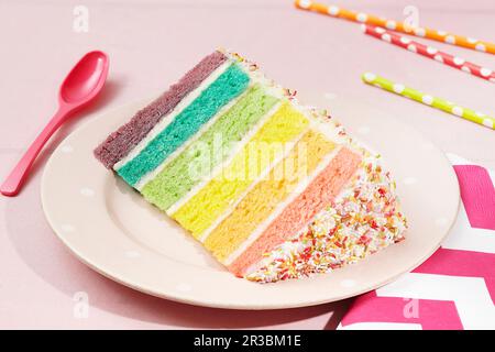 Une tranche de gâteau arc-en-ciel couvert de saupoudrer sur une assiette Banque D'Images