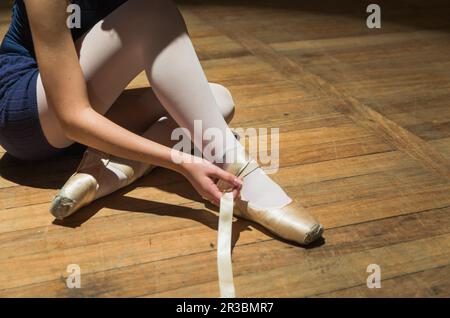 Ballerine jeune ou danseuse mettant des pantoufles de ballet sur un plancher de théâtre en bois Banque D'Images