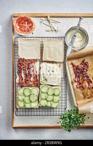 Préparation de sandwichs club avec du bacon, du concombre et des tomates Banque D'Images