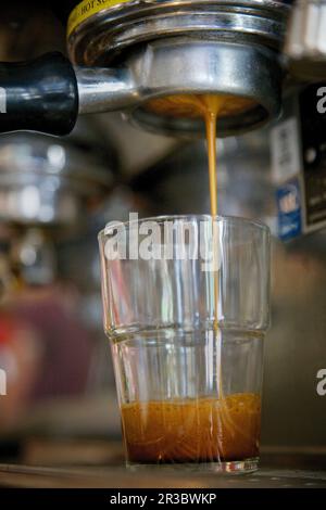 Gros plan de l'espresso s'écoulant d'un porte-filtre sans fond dans une tasse en verre Banque D'Images