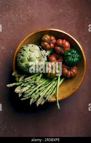 Tomates, artichauts et asperges dans un bol en grès Banque D'Images