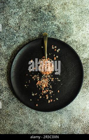 Concept de cuisson avec cuillère vintage avec sel rose sur plaque en bois noir Banque D'Images