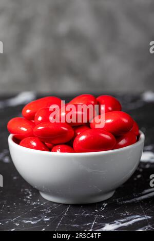 Chocolat et dragee aux amandes. Dragee au chocolat rouge dans un bol en céramique sur fond sombre. Gros plan Banque D'Images