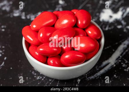 Dragee d'amande au chocolat. Dragee au chocolat rouge dans un bol en céramique sur fond sombre. Gros plan Banque D'Images