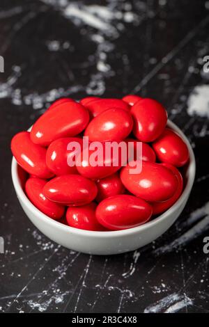 Chocolat et dragee aux amandes. Dragee au chocolat rouge dans un bol en céramique sur fond sombre Banque D'Images