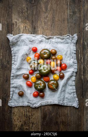 Mélange de variétés de tomates sur un torchon à vaisselle en lin, sur une surface en bois Banque D'Images