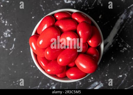 Dragee d'amande au chocolat. Dragee au chocolat rouge dans un bol en céramique sur fond sombre. Vue de dessus Banque D'Images