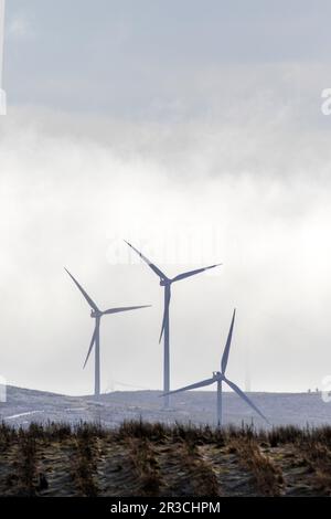 Trois éoliennes qui se manifestent à travers la brume, avec un jet de neige légère, dans les collines écossaises. Banque D'Images