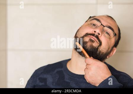 Homme en lunettes peignez sa barbe à l'intérieur Banque D'Images