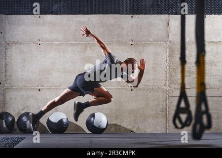 Un homme musclé capturé dans l'air alors qu'il saute dans une salle de sport moderne, mettant en valeur son athlétisme, sa puissance et sa détermination grâce à une forme physique de haute intensité Banque D'Images
