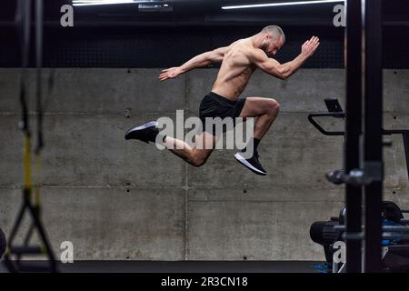 Un homme musclé capturé dans l'air alors qu'il saute dans une salle de sport moderne, mettant en valeur son athlétisme, sa puissance et sa détermination grâce à une forme physique de haute intensité Banque D'Images