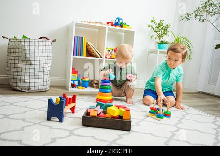 Enfants jouant avec des jouets en bois assis sur un sol Banque D'Images