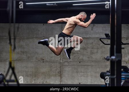 Un homme musclé capturé dans l'air alors qu'il saute dans une salle de sport moderne, mettant en valeur son athlétisme, sa puissance et sa détermination grâce à une forme physique de haute intensité Banque D'Images
