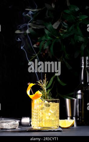 Boisson cocktail à la pénicilline avec scotch, whisky, sirop, jus de citron et glace en verre avec zeste d'orange, garni de romarin à la vapeur. Backgro noir Banque D'Images