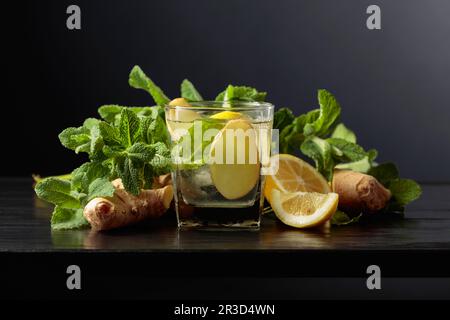 Boisson rafraîchissante froide avec glace, gingembre, citron et menthe sur fond noir. Banque D'Images