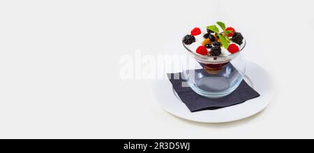 Dessert aux baies et aux glaces dans un bol en verre transparent sur une assiette blanche sur fond blanc Banque D'Images