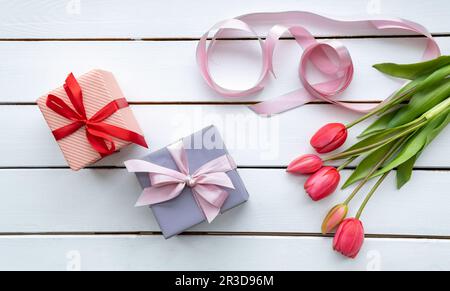 Boîte cadeau avec long ruban rose et tulipes sur fond clair Banque D'Images