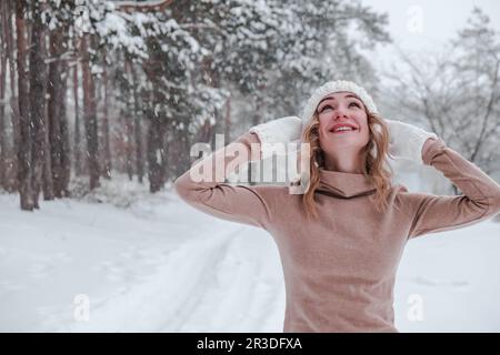 Noël, les vacances et la saison concept. Jeune femme heureuse soufflant de la neige dans la nature de la forêt d'hiver. Vêtements chauds gants tricotés Banque D'Images