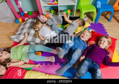 Les enfants actifs s'assetent sur des oreillers et des tapis moelleux à la maternelle Banque D'Images