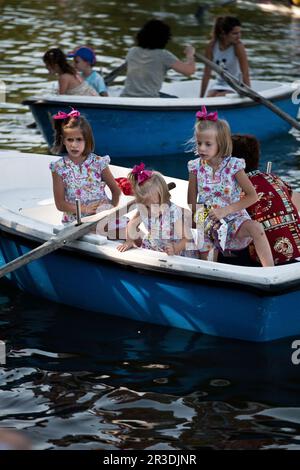 Trois sœurs, vêtues comme elles, nourrissant le poisson de l'étang du parc Buen Retiro de Madrid à partir d'un bateau à rames. Madrid, Espagne. Banque D'Images