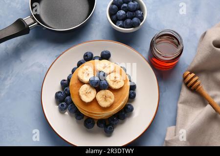 Assiette avec crêpes sucrées, miel et poêle sur fond bleu Banque D'Images