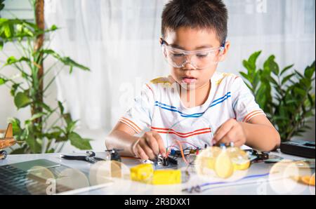 Un enfant asiatique branche le câble d'énergie et de signal à la puce de capteur avec la voiture robot Arduino Banque D'Images