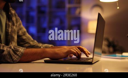 Un jeune étudiant arabe travaille sur son ordinateur portable le soir dans le salon. Un homme avec une barbe travaille dans ELLE de la maison, tapote sur le clavier, écrit Banque D'Images