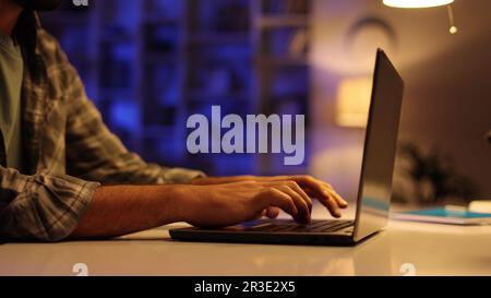 Un jeune étudiant arabe travaille sur son ordinateur portable le soir dans le salon. Un homme avec une barbe travaille dans ELLE de la maison, tapote sur le clavier, écrit Banque D'Images