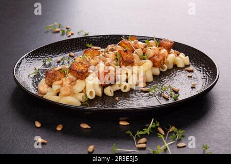 Délicieuses pâtes aux pois chiches, tofu frit et herbes fraîches sur une assiette noire. Banque D'Images