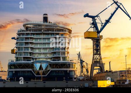 Vue panoramique arrière Grand paquebot de croisière moderne de luxe sous construction grues sur le quai à sec du port de Hambourg spectaculaire coucher de soleil ciel Banque D'Images