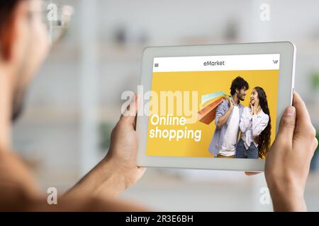 Jeune homme utilise une tablette numérique moderne avec boutique de mode à l'écran, rognée, application mobile à la maison ou au bureau Banque D'Images